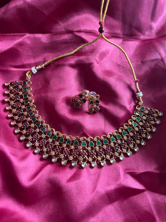 Ornate necklace with green and red stones on a pink fabric background